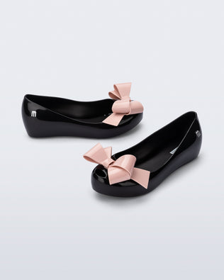 Top and side angled view of a pair of black Ultragirl Classy kids ballerina flats with pink bow