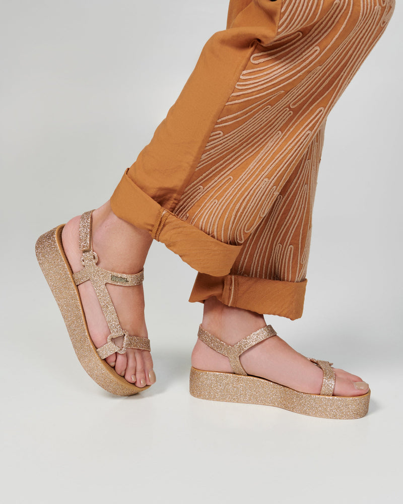 Model's legs in beige pants wearing a pair of beige glitter Sun Downton Platform sandals