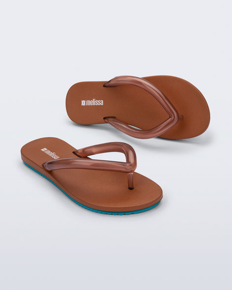 Top and angled view a pair of brown Flip Flop Airflow sandal with a clear brown strap and blue bottom