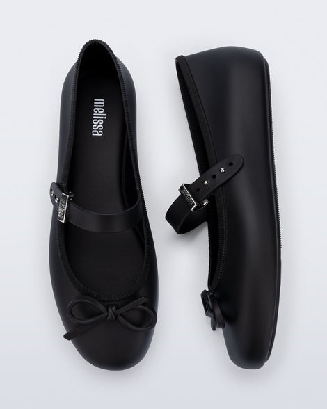 Side and top view of a pair of black Soft Ballerina Delicate Bow flats with top strap and bow