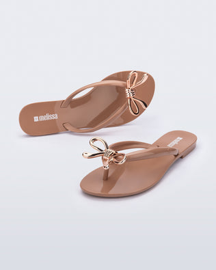 Top and angled view of a pair of brown Harmonic Iris flip flops with rose gold bow