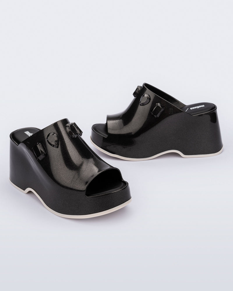 Angled and side view of a pair of metallic black Patty Stones + Undercover platform open toe mules with beige sole and stone embellishments on upper.