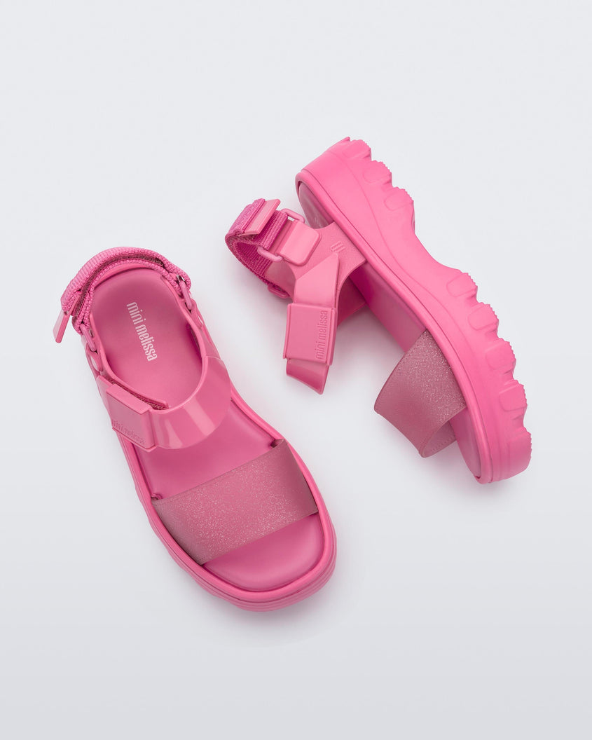 Top and side view of a pair of Mini Melissa Kick Off platform sandals in pink with adjustable velcro ankle straps 
