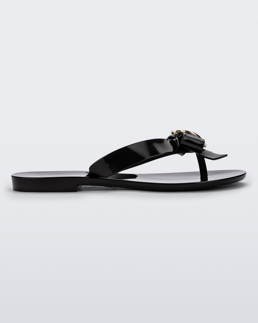 Side view of a black Melissa Harmonic Heart flip flop with a black bow and gold heart detail on the straps