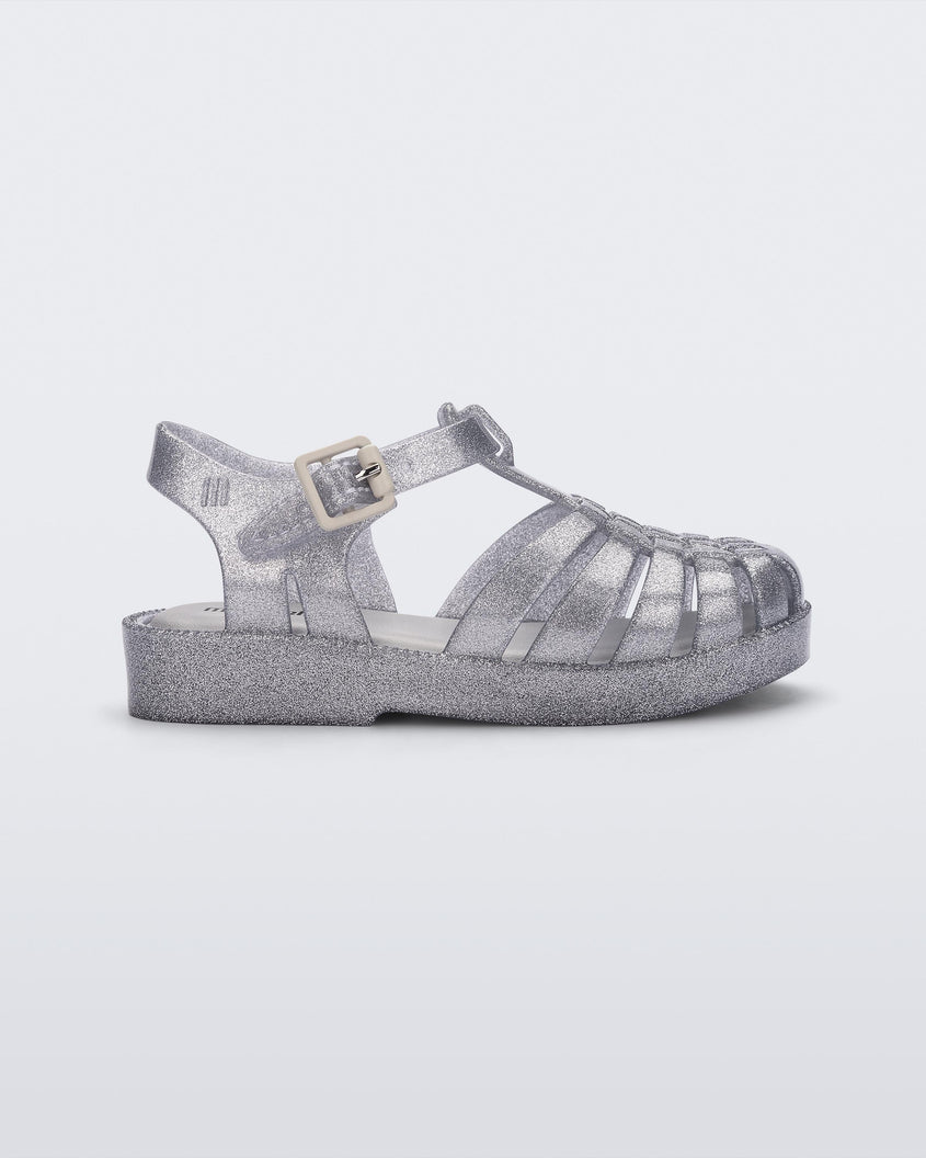 Side view of a Mini Melissa Possession baby sandal in glitter clear with velcro buckle closure on the ankle strap