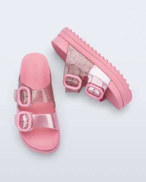 Side and top view of a pair of pink Cozy Platform kids slides with two straps with buckles, one clear glitter the other pearly pink