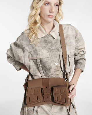 Model in a beige outfit with a brown Cargo bag with two small pockets on the front and an adjustable strap with measurements of the bag: 28cm x 6cm x 17cm