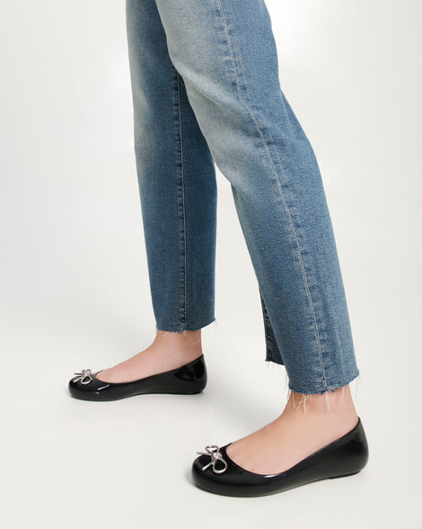 Model's legs wearing a pair of black Sweet Love Chrome flats with silver bow