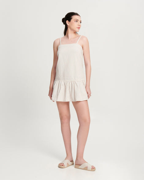 Model in a white dress wearing a pair of beige Cozy Cross sandals with crisscross top straps