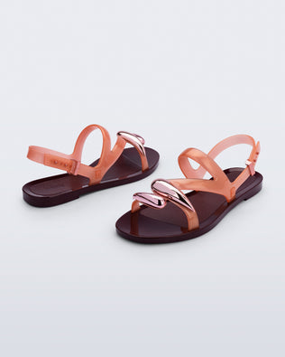 Back and angled view of a pair of orange Iris sandals with burgundy sole and rose gold upper embellishments