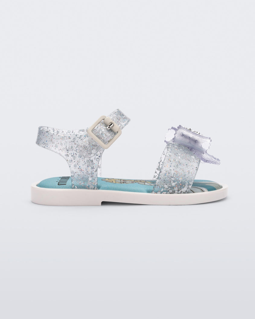 Side view of a glitter clear Mini Melissa Mar Sandal Princess sandal with a snowflake bow detail on the front strap, an ankle strap and Princess Elsa soul