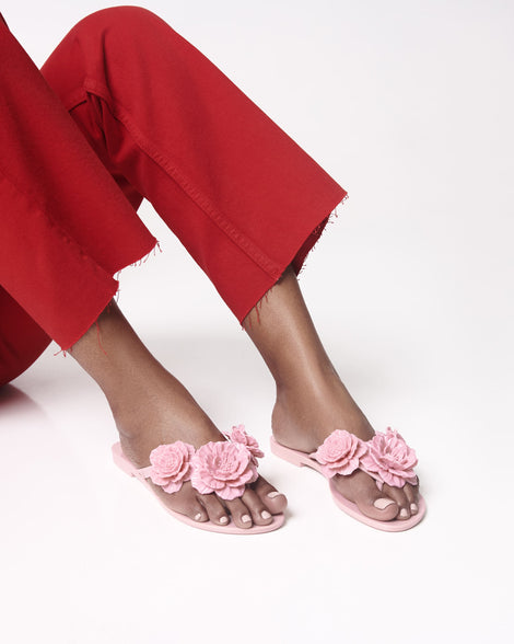 Model's legs in red pants wearing a pair of pink Harmonic Springtime women's flip flop with 3 pink flowers.