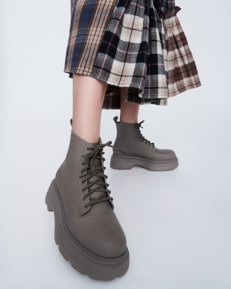 Model's legs in a brown plaid skirt wearing a pair of matte brown Coturno Soft Platform boots