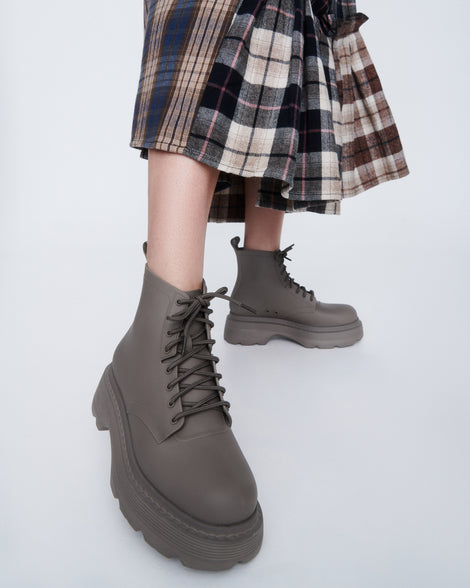 Model's legs in a brown plaid skirt wearing a pair of matte brown Coturno Soft Platform boots