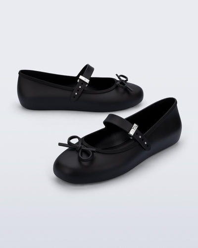Side and angled view of a pair of black Soft Ballerina Delicate Bow flats with top strap and bow