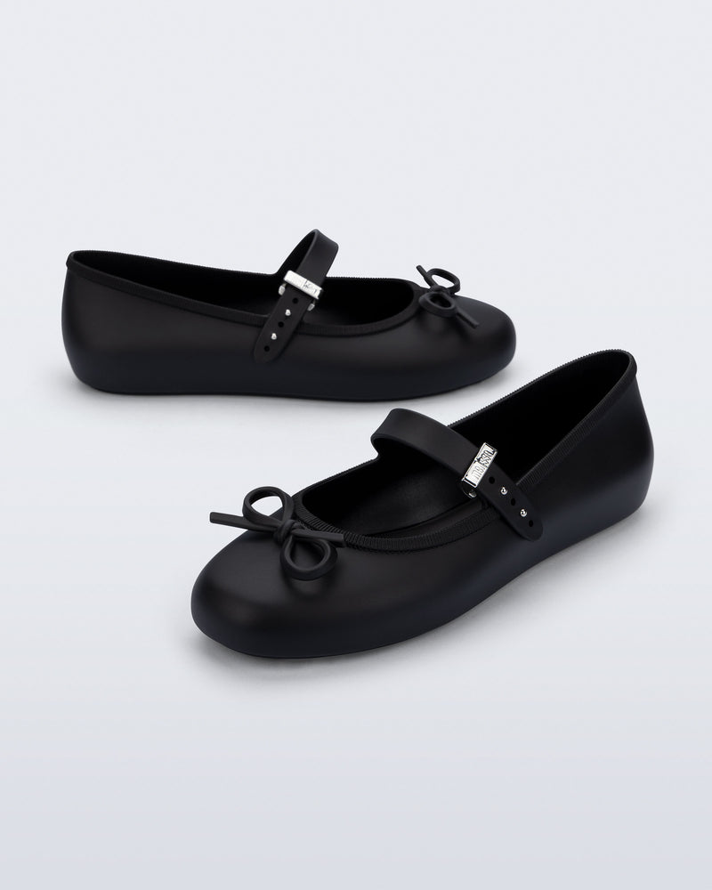 Side and angled view of a pair of black Soft Ballerina Delicate Bow flats with top strap and bow
