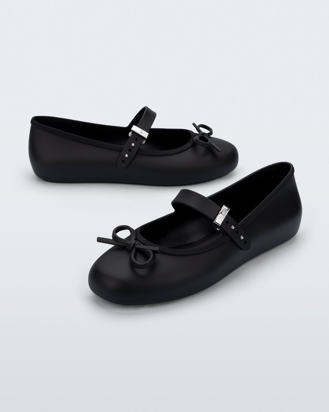 Side and angled view of a pair of black Soft Ballerina Delicate Bow flats with top strap and bow