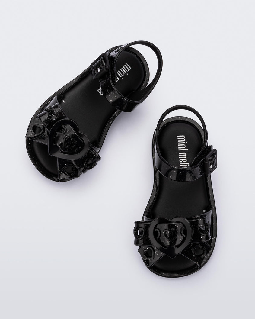 A top view of a pair of glitter black Mini Melissa Mar Sandal Heart sandals with a glitter black heart bow detail on the front strap and an ankle strap