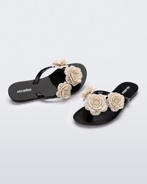 Angled view of a pair of a black Harmonic Springtime kids flip flop with three beige flowers.