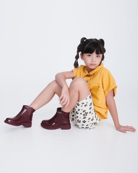 Child model in a yellow shirt and beige shorts wearing a pair of burgundy Chelsea II kids boots