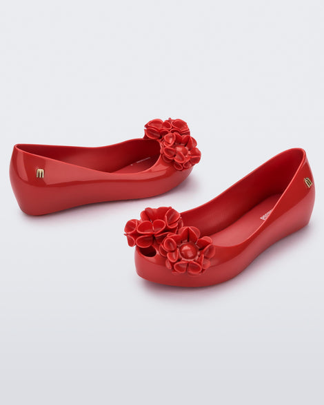 Angled view of a pair of a red Ultragirl Springtime kids flat with two red flowers and peep toe.