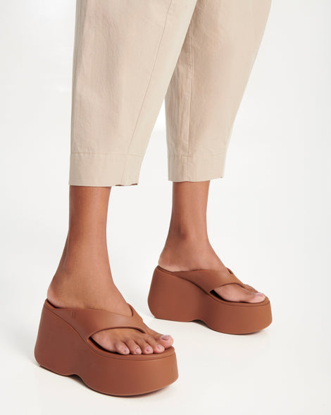 Model's legs wearing a pair of brown Free Thong Wedge platform flip flop sandals