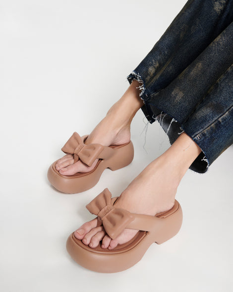 Model's legs wearing a pair of brown Free Fuzzy Platform flip flops