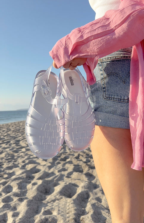 Model holding the clear possession sandal on a beach