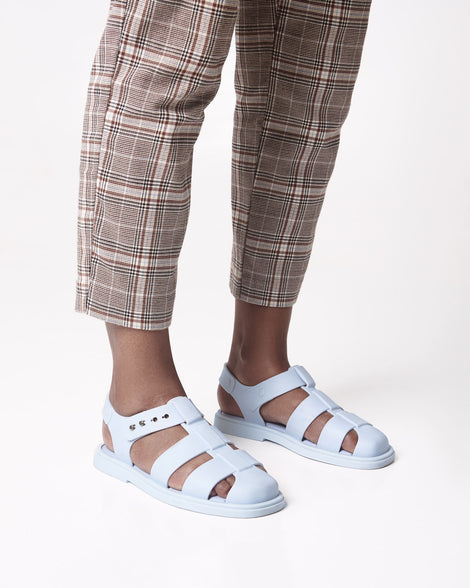 Model's legs in brown plaid  pants wearing a pair of blue Emma women's sandals.