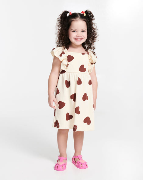 Child model in a beige dress with hearts wearing a pair of pink Hip Heart Ballerina baby sandals with heart on front