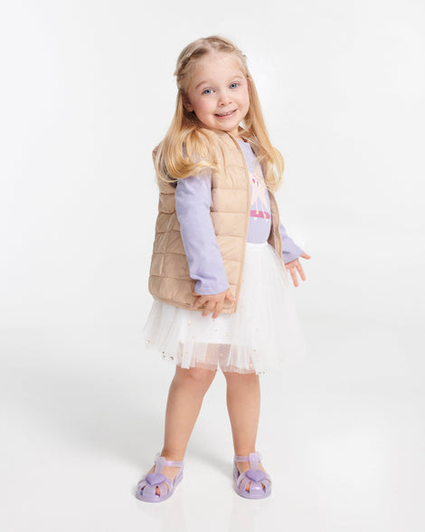 Child model in a white skirt wearing a pair of lilac Hip Heart Ballerina baby sandals with heart on front