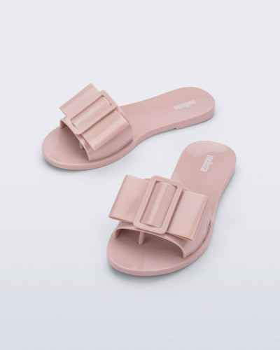 Top and side view a pair of light pink Babe slide sandals with large bow on top.