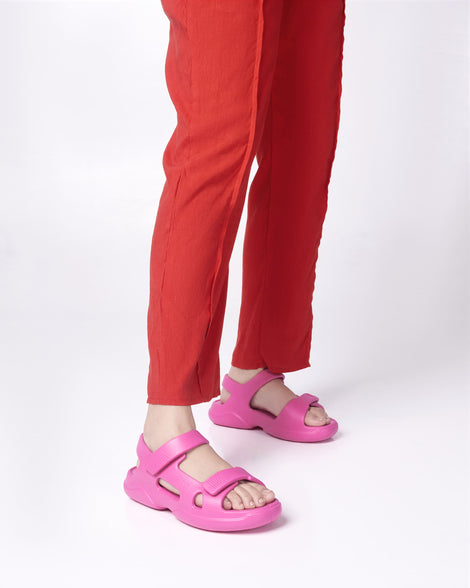 Model's legs in red pants wearing a pair of pink Free Papete sandals.