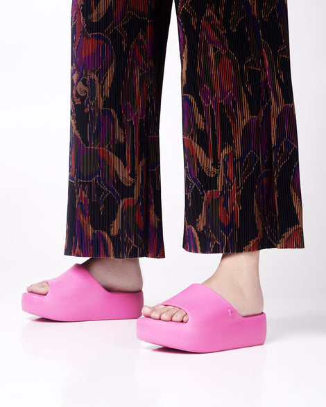 Model's legs in black patterned pants wearing a pair of pink Free Platform women's slides