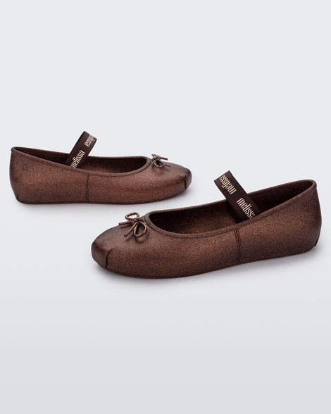 Angled view of a pair of Melissa Sophie ballet flats in bronze with M-logo strap and bow applique