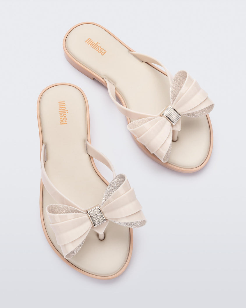 Overhead view of a pair of Melissa slim strap flip flops in light beige with bow applique