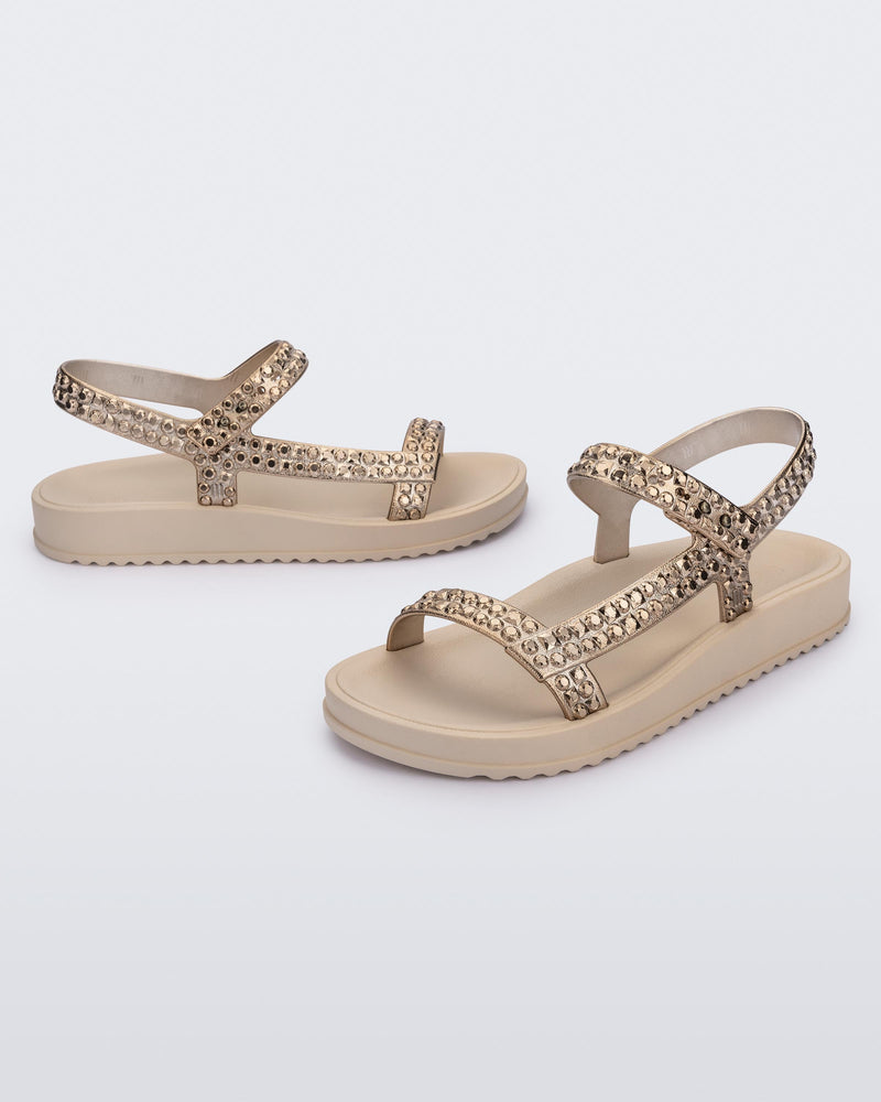 Side and angled view of a pair of beige Lust sandals with gold strap