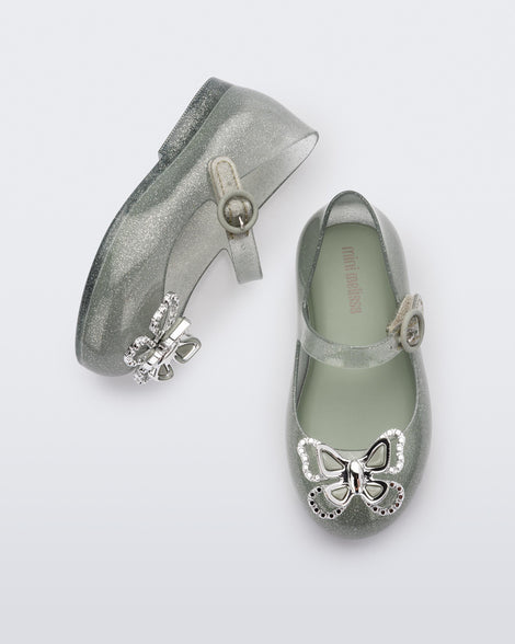 A top and side view of a pair of glitter green Mini Melissa Sweet Love Butterfly flats with a top strap and a silver butterfly detail on the toe