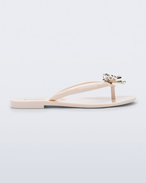 Side view of a beige Harmonic Iris flip flop with gold bow