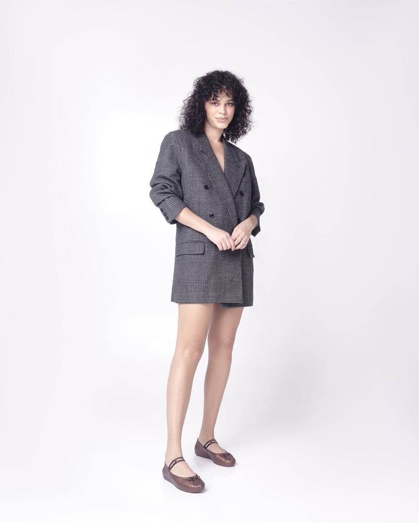 Model posing in a blazer dress wearing a pair of Melissa Sophie ballet flats in bronze with M-logo strap and bow applique