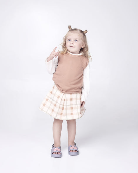 Toddler model in a pink shirt and pink and white plaid skirt wearing a pair of grey Free Cute baby sandals with hippo face on front upper 