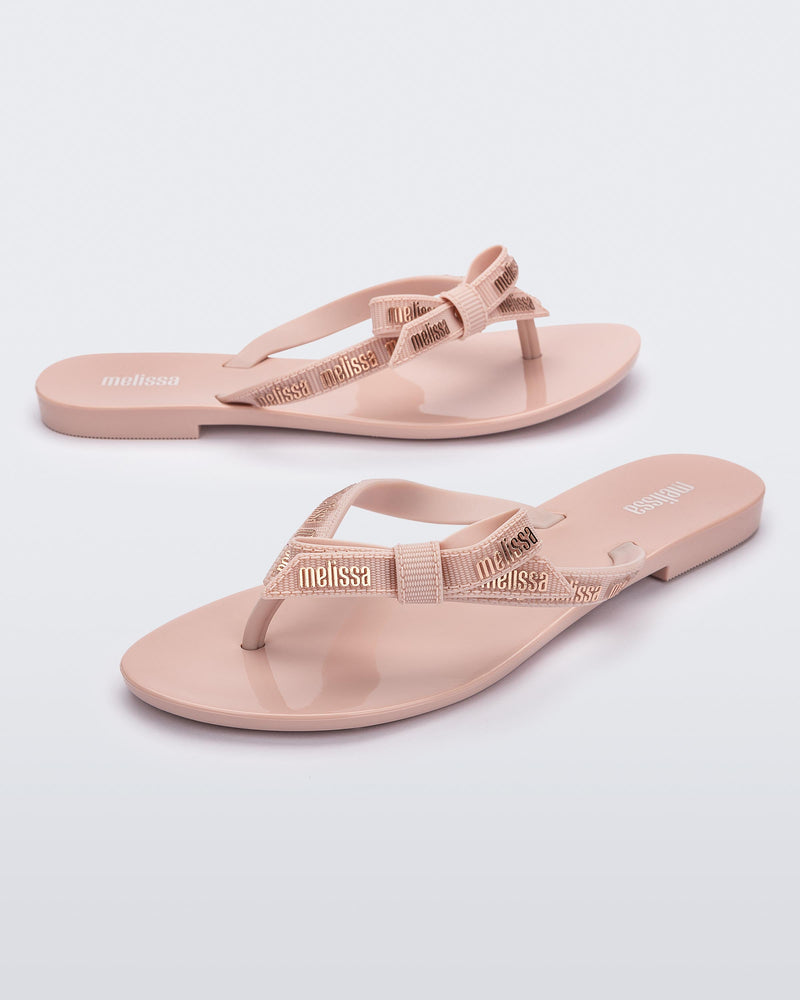 Angled view of a pair of light pink Harmonic M Lover adult flip flop with Melissa logo on strap