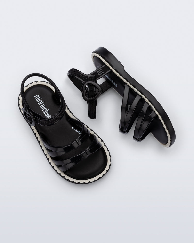 Side and top view of a pair of black Aurora baby sandals with beige trim