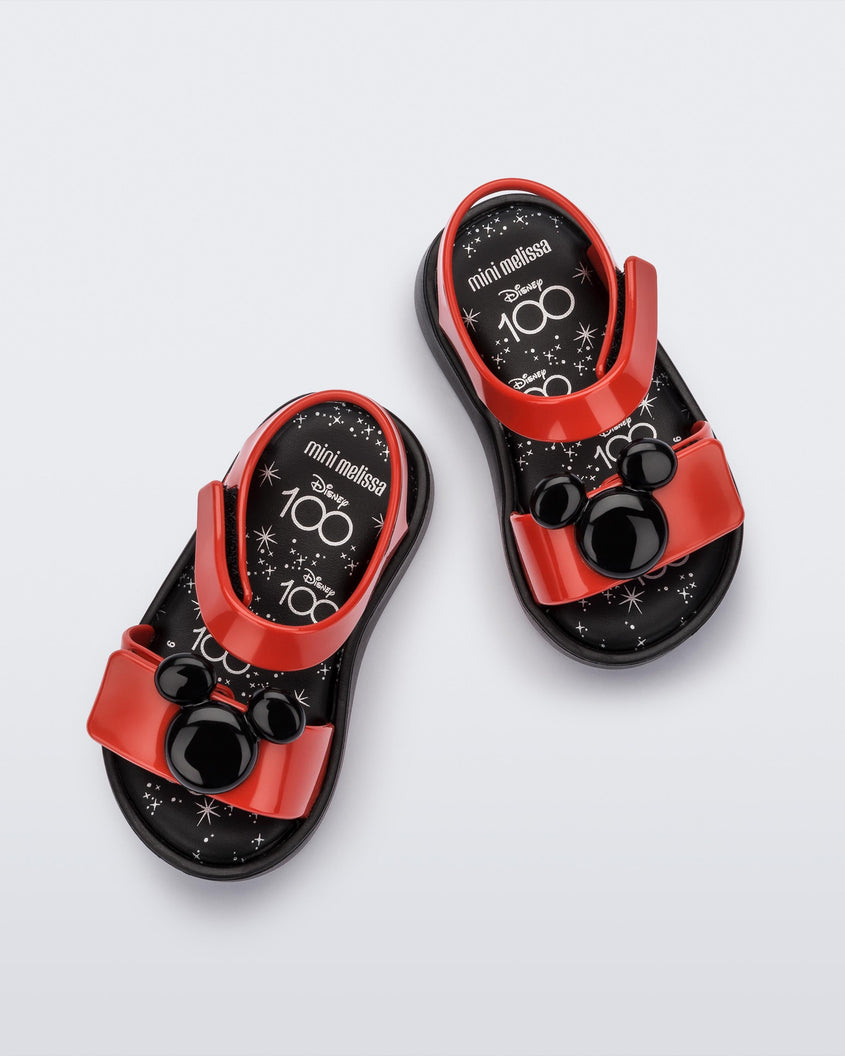 A top view of a pair of red/black Mini Melissa Jump sandals with a black Mickey Mouse logo detail on the front red strap and a red ankle strap