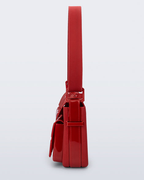 Side view of a red Cargo bag with two small pockets on the front and an adjustable strap