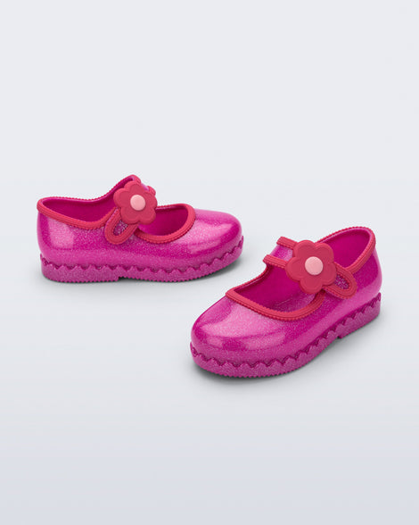 Side and angled view of a pair of glitter pink Hip Ballerina baby flats with flower on strap
