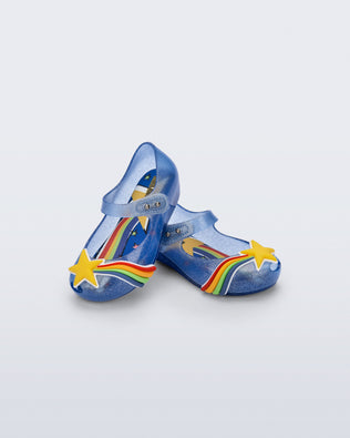 Angled view of a pair of glitter blue Ultragirl Colors baby flats with yellow star and rainbow on top