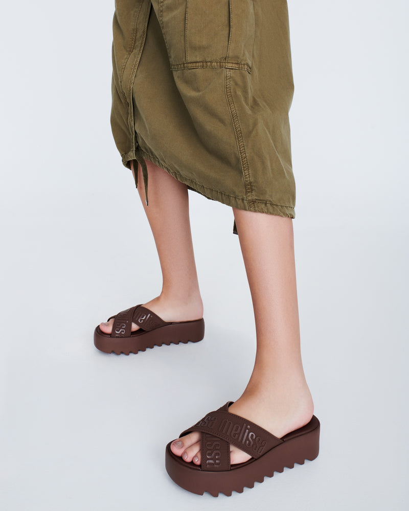 Model's legs wearing a pair of brown M Lover Cross Strap platform slides
