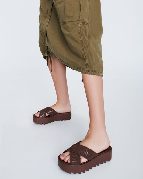 Model's legs wearing a pair of brown M Lover Cross Strap platform slides