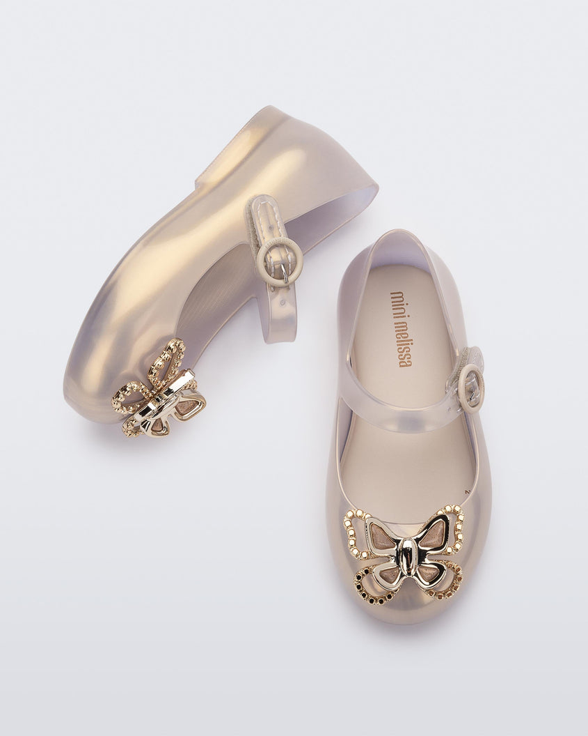 A top and side view of a pair of pearly gold Mini Melissa Sweet Love Butterfly flats with a top strap and a gold butterfly detail on the toe